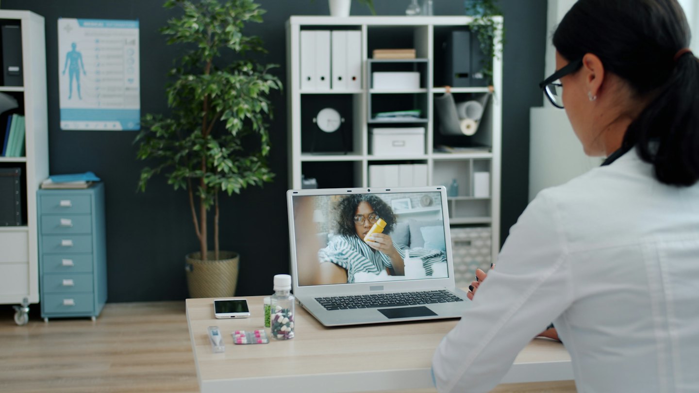 Arzt im Telehealth-Gespräch mit Patient, der eine gelbe Pillenflasche hält.