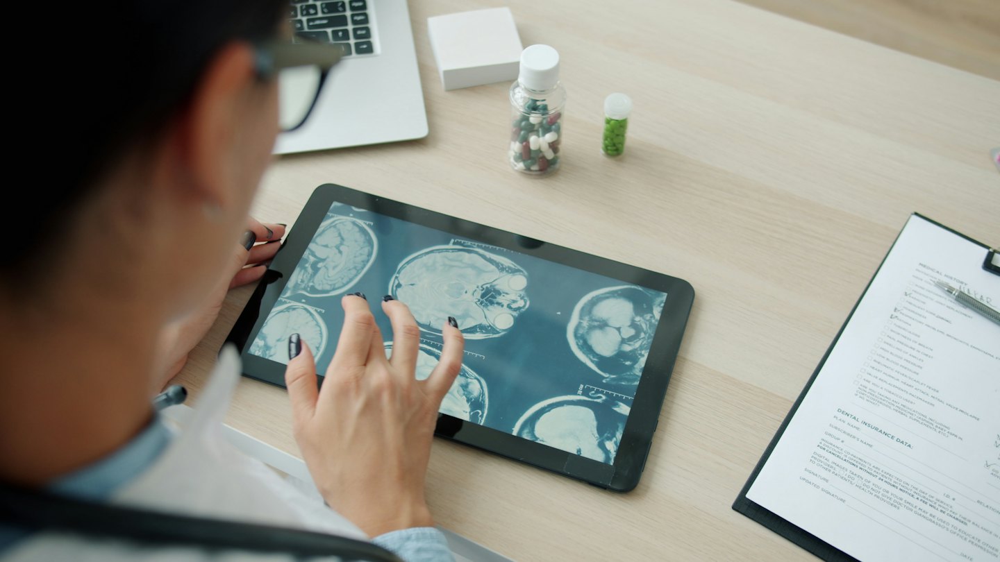 Arzt, der am Schreibtisch Gehirnscans auf einem Tablet überprüft.